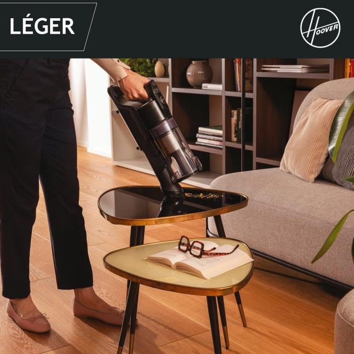 Una persona aspira briciole da un tavolo con un aspirapolvere Hoover senza fili.