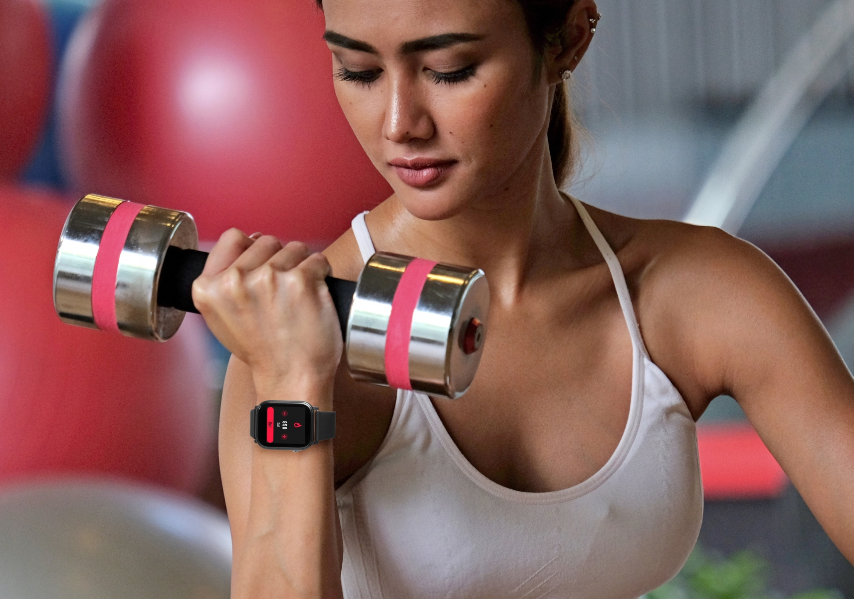 Donna solleva un manubrio, indossa uno smartwatch in palestra.