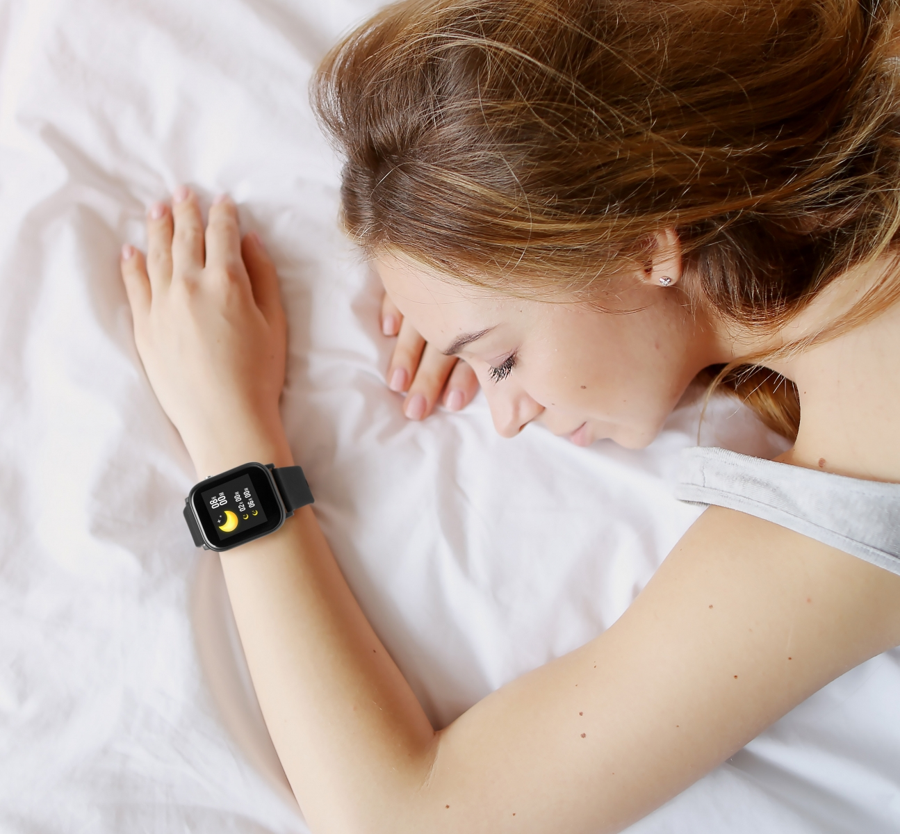 Una donna dorme su un letto bianco. Indossa uno smartwatch.
