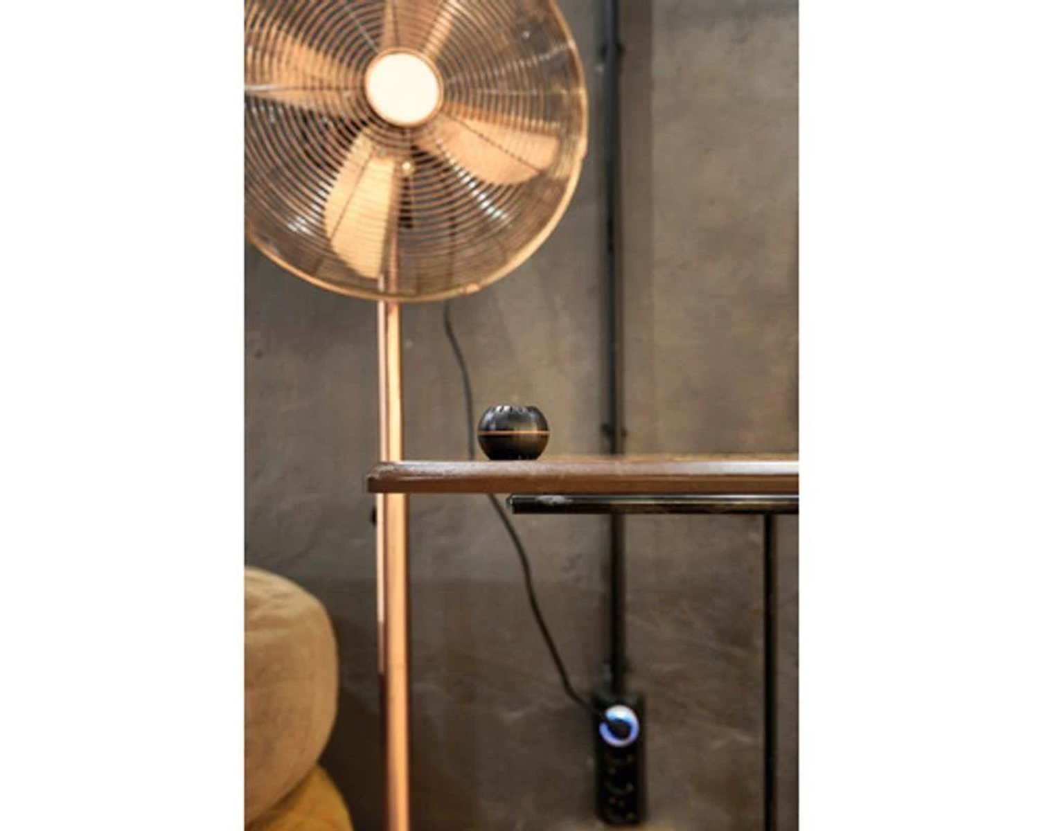 Un ventilatore accanto a una mensola con una piccola sfera nera.