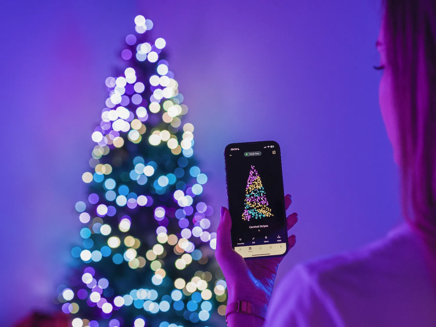 Osoba trzyma smartfon wyświetlający kolorowe wzory świateł, z rozmytą, podświetloną choinką w tle.