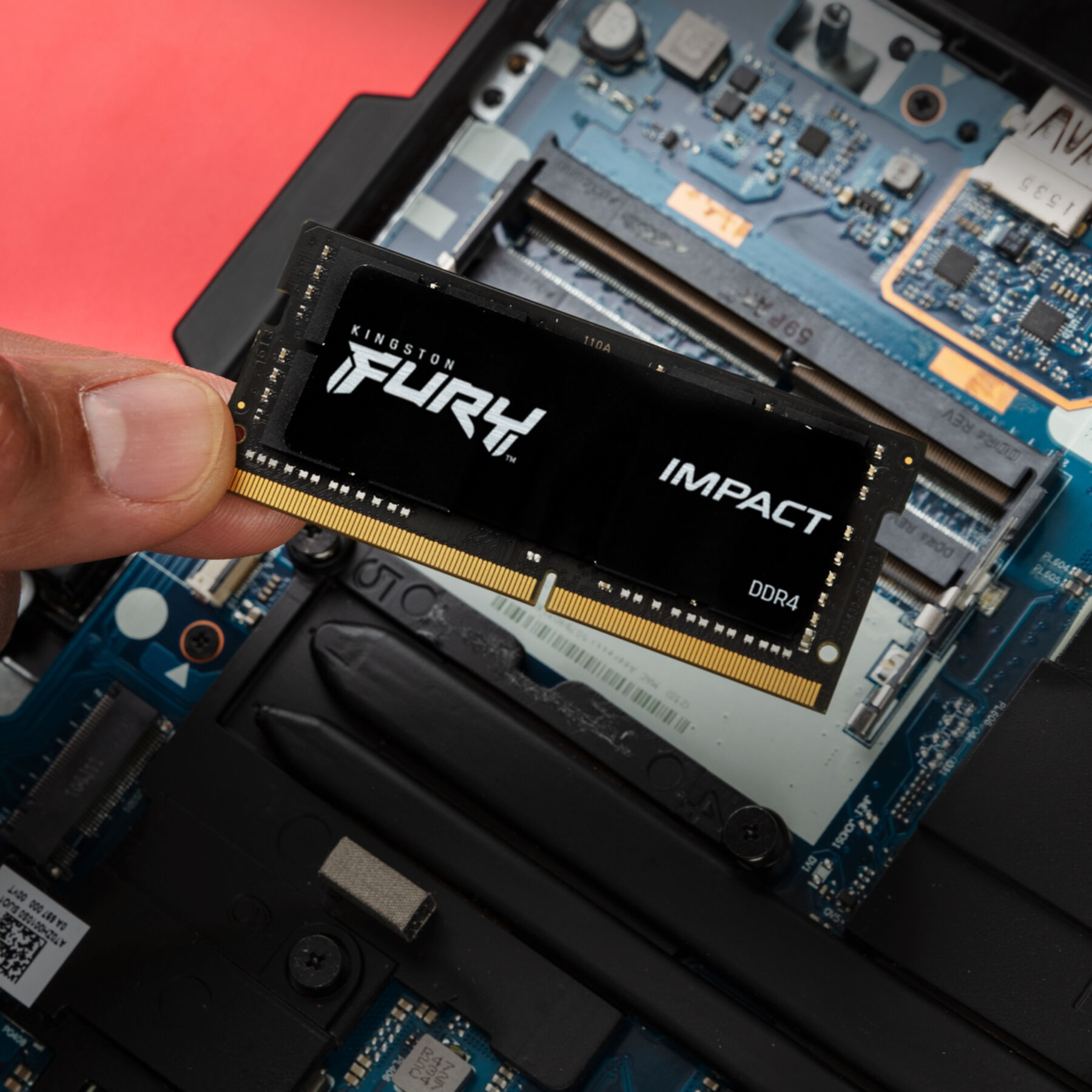 Dłoń trzyma moduł RAM Kingston FURY Impact DDR4 nad płytą główną laptopa.
