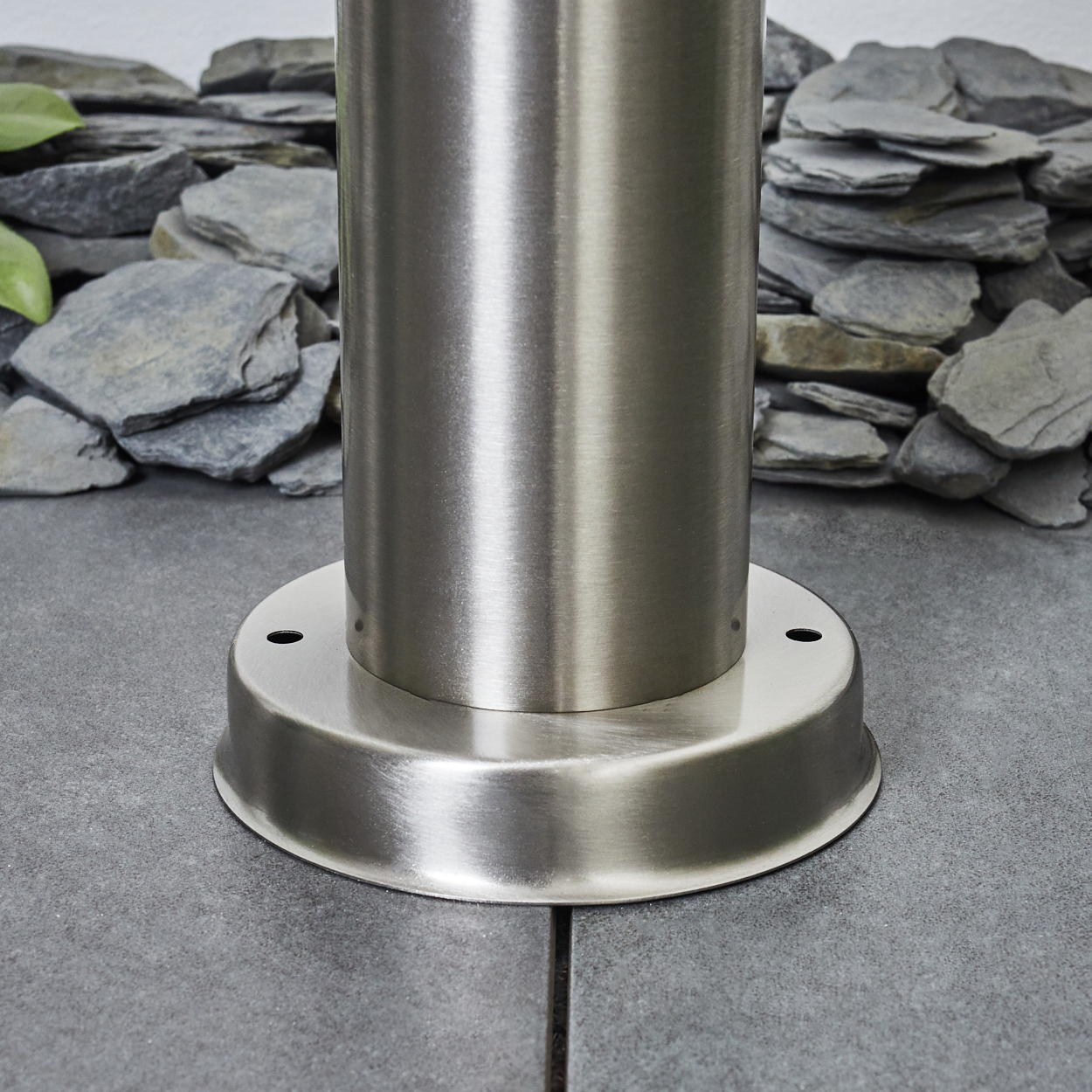 Ein silberner Metallpfosten steht auf einem grauen Steinboden, hinter ihm sind Schiefersteine.