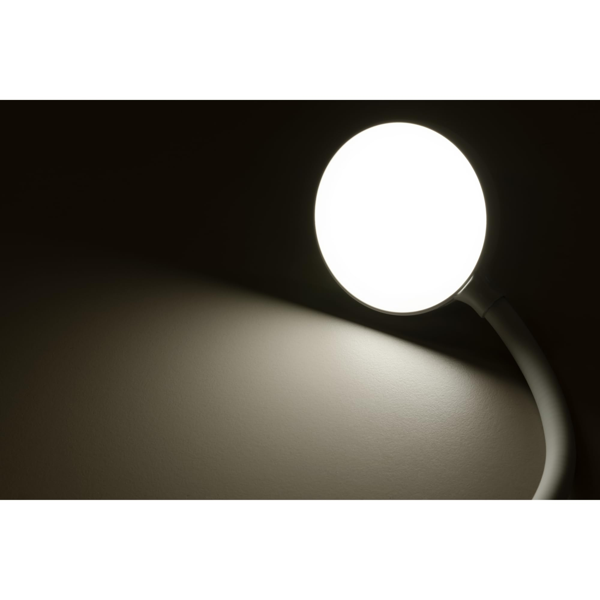 Eine helle, runde Lampe beleuchtet eine Wand, die von Dunkelheit umgeben ist.