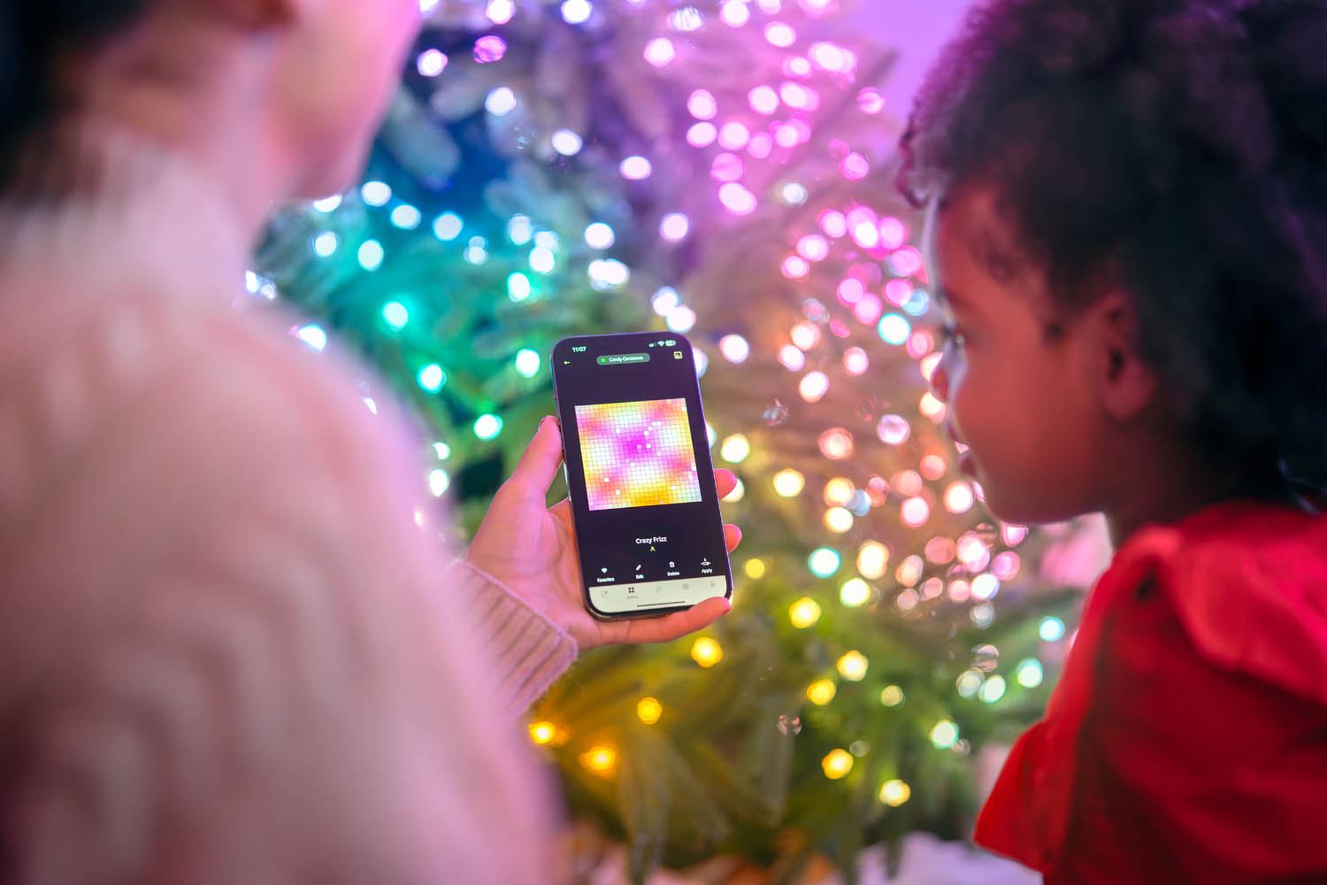 Persona tiene uno smartphone davanti a un albero di Natale con luci colorate.