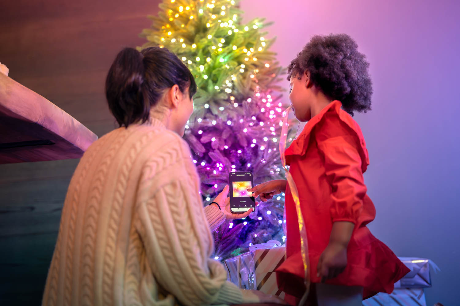 Due persone controllano una catena di luci colorate su un albero di Natale con uno smartphone.
