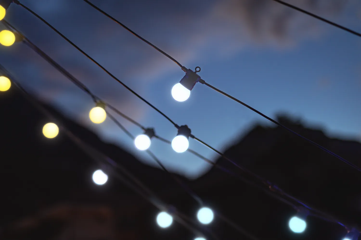 Lampki sznurkowe świecą o zmierzchu na tle ciemnego nieba i gór.