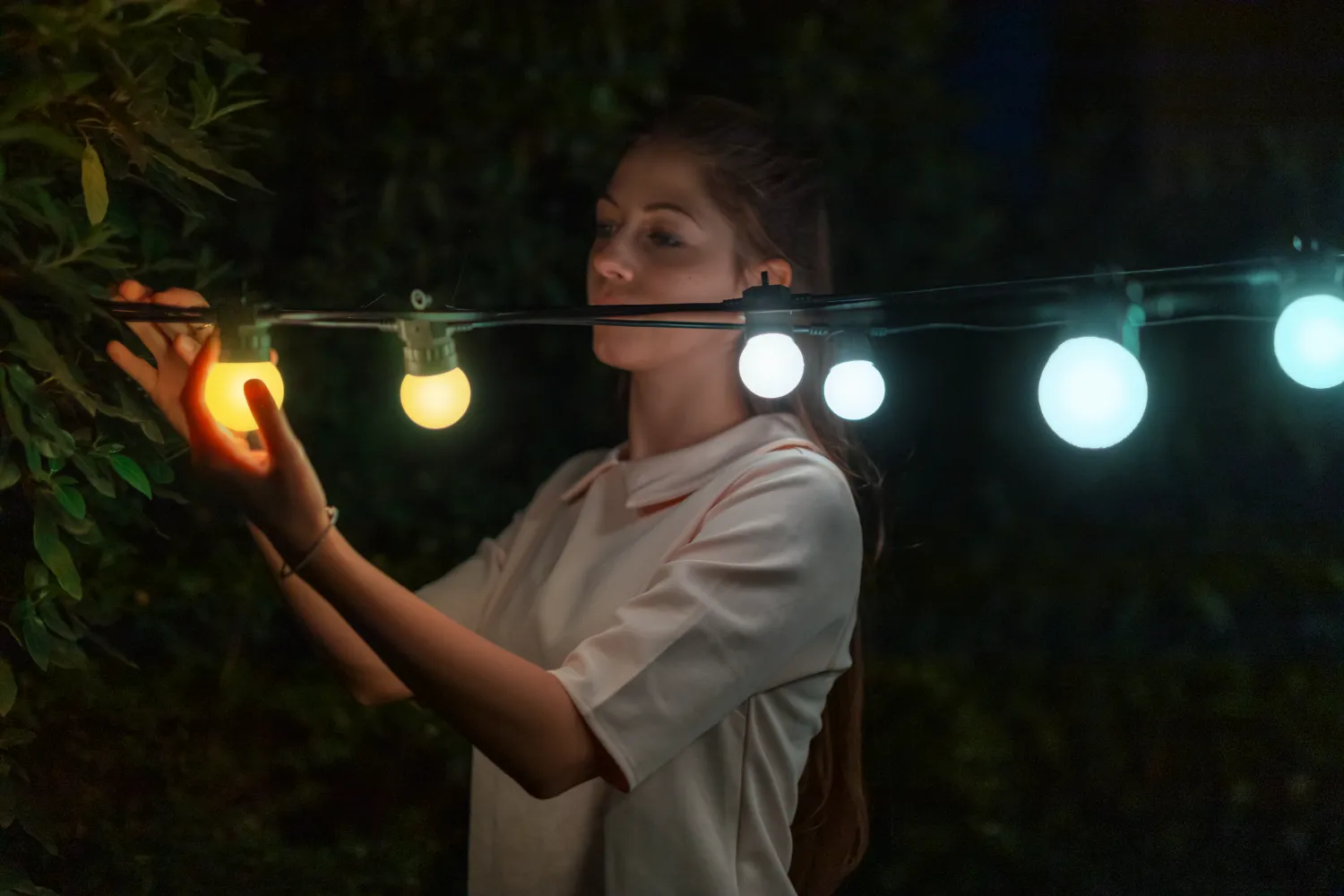 Kobieta wiesza w ciemności sznur świateł z żółtymi i białymi żarówkami.