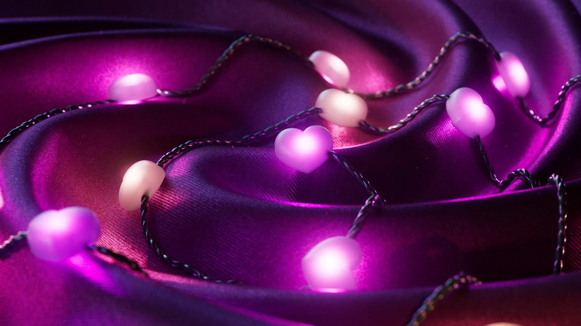 Fioletowa satyna z lampkami w kształcie serca: Girlanda świetlna na błyszczącym materiale.