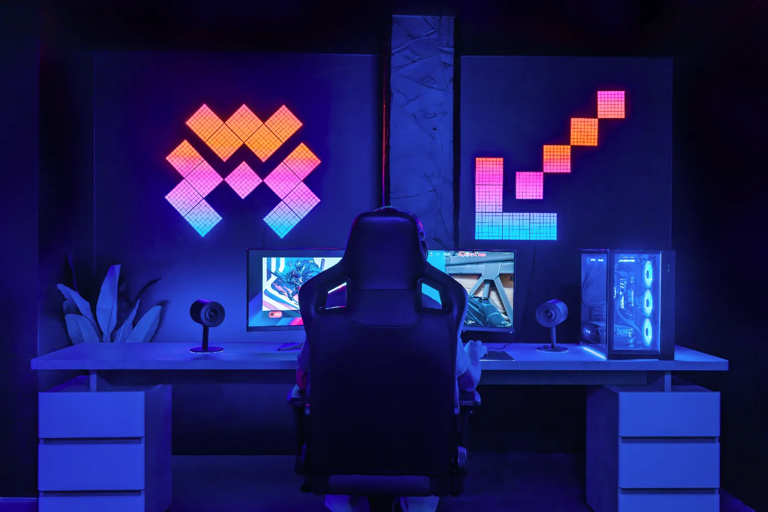 Gracz siedzi przed dwoma monitorami w pokoju z neonami i kolorowymi panelami ściennymi.