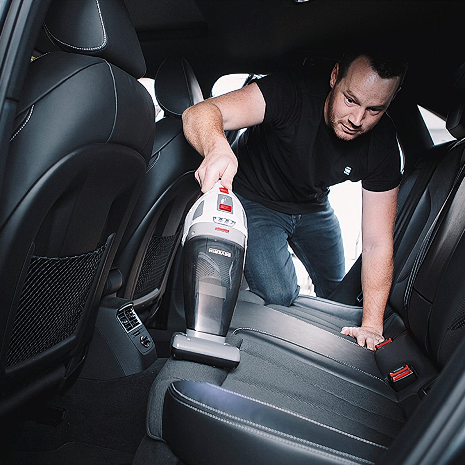Mężczyzna odkurza siedzenia samochodu odkurzaczem.
