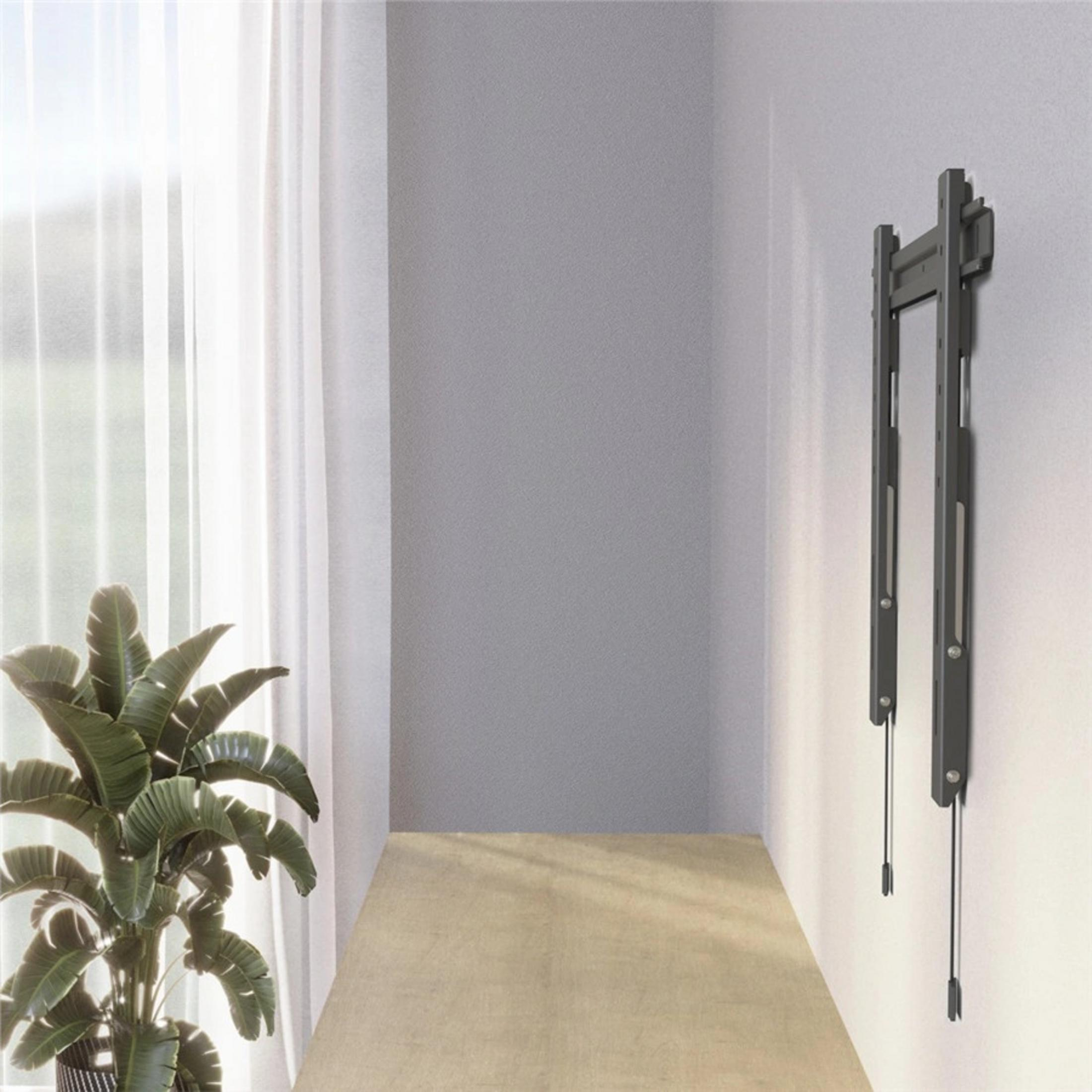 Ein dunkler Wandhalter für Fernseher hängt an einer weißen Wand neben einem Fenster.