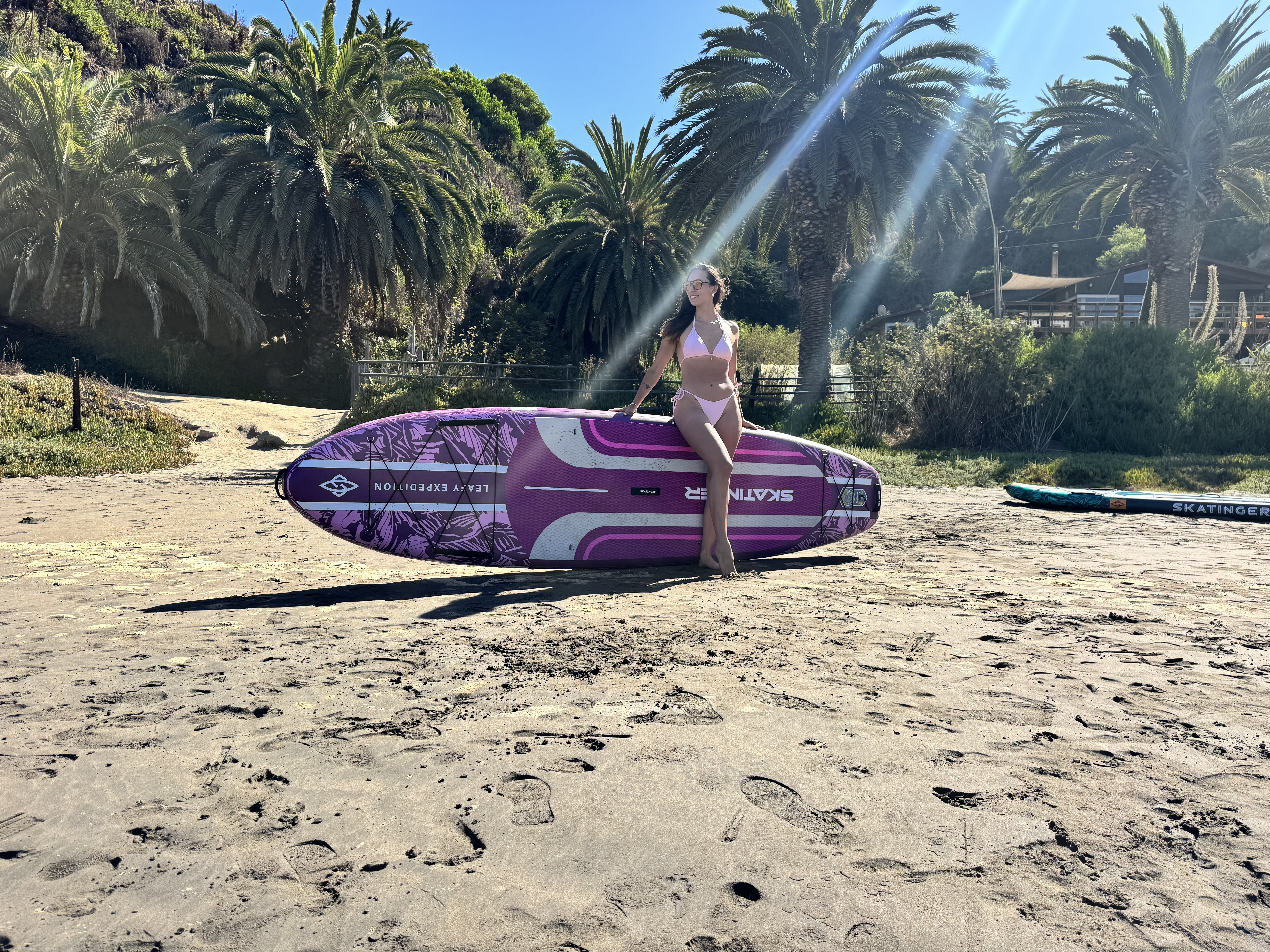 Kobieta w bikini siedzi na desce SUP na plaży.