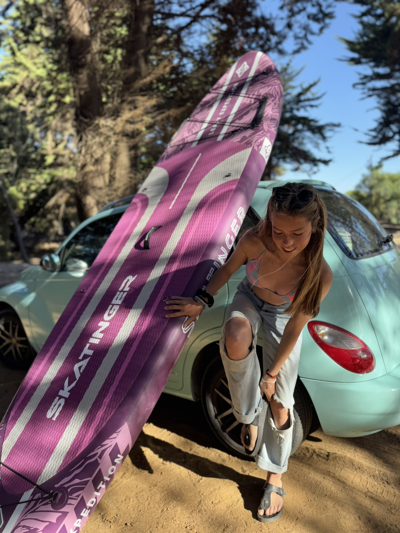 Dziewczyna z fioletową deską SUP obok turkusowego samochodu na zewnątrz.