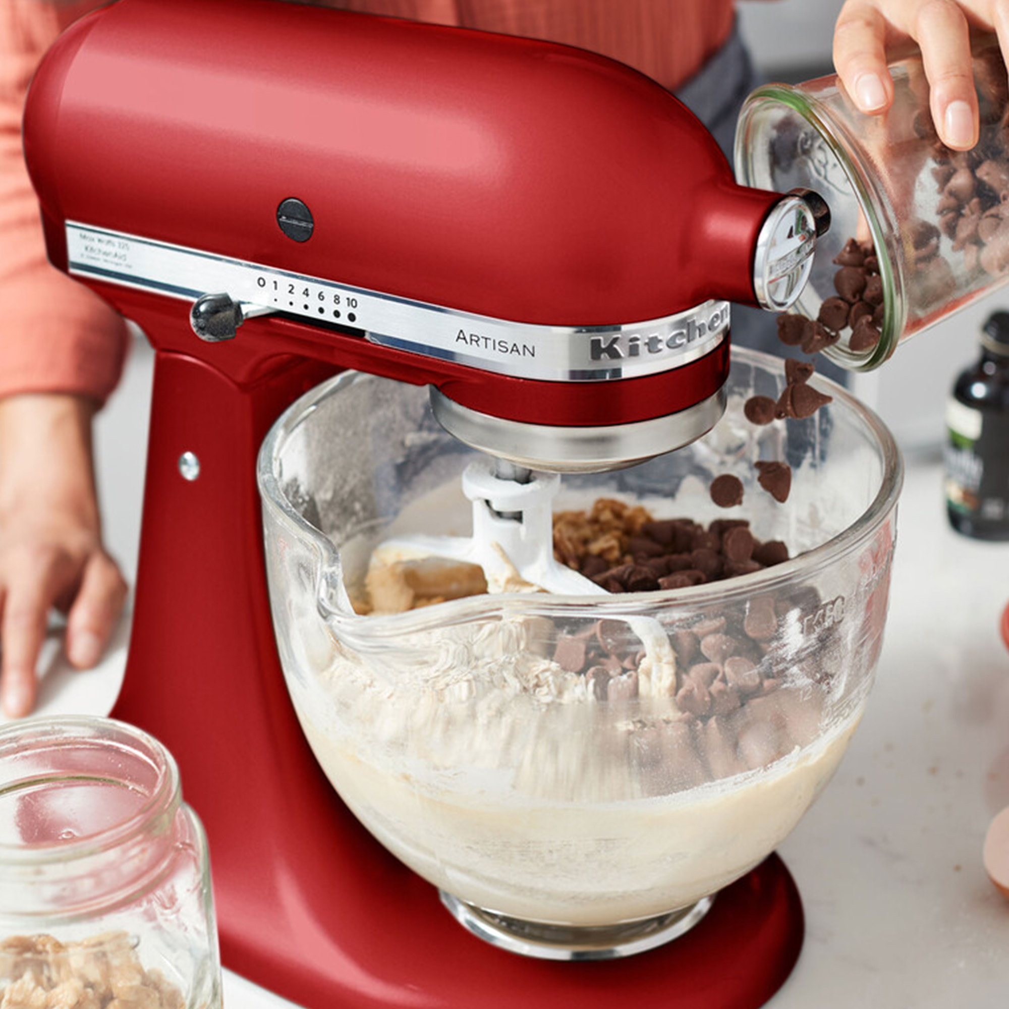 Czerwony mikser planetarny dodaje czekoladowe chipsy do ciasta w szklanej misie.