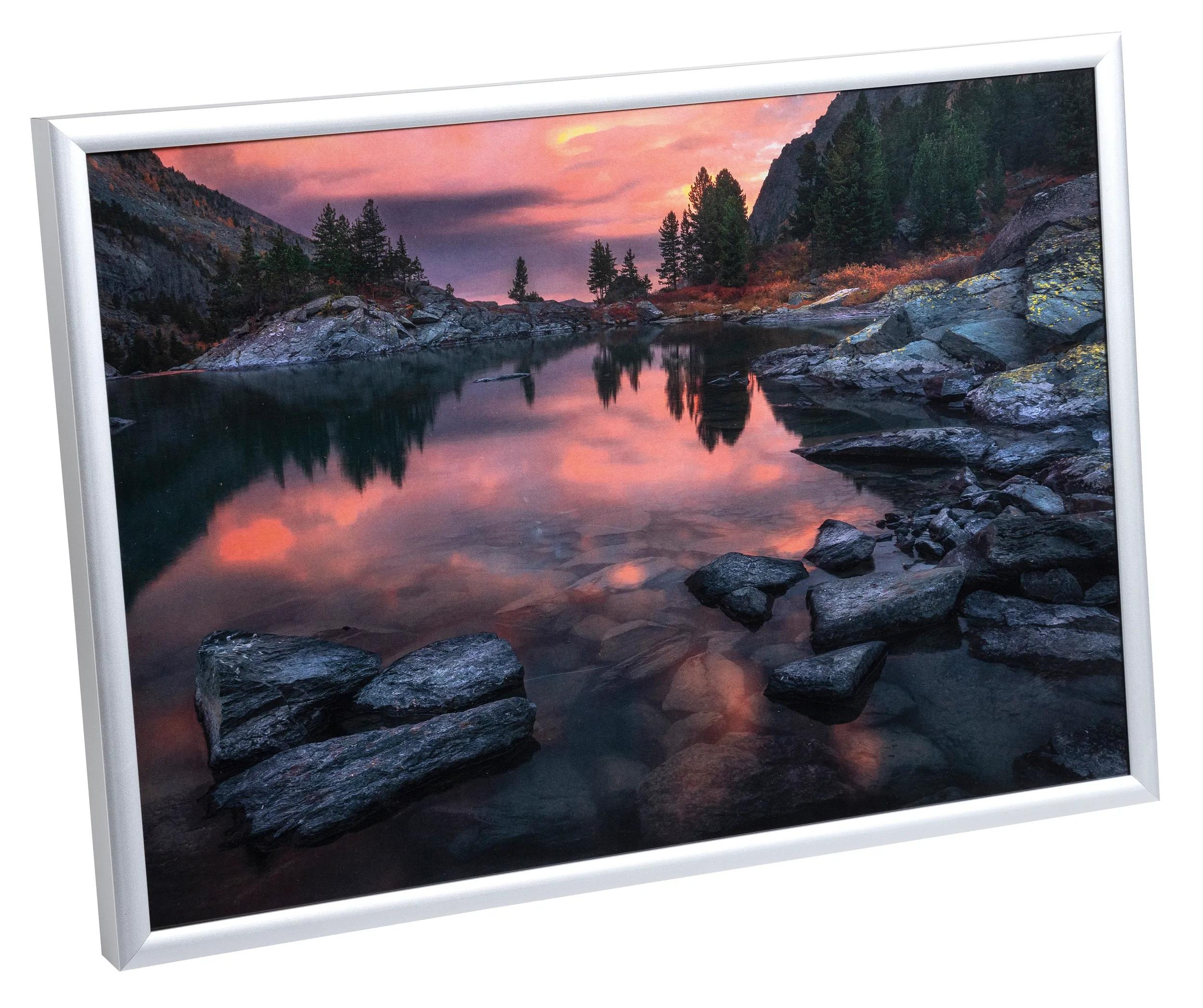 Lago de montaña al atardecer con nubes y árboles reflejados en el agua.
