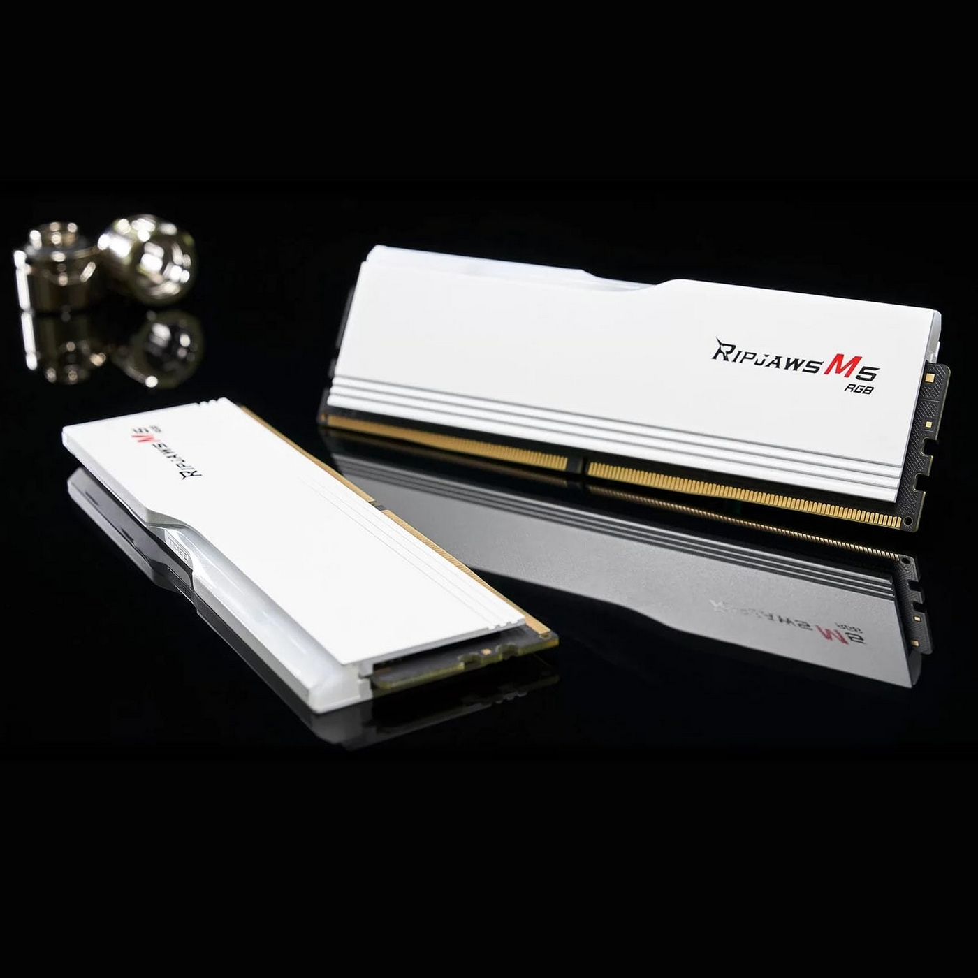 Dwa białe moduły RAM Ripjaws M5 RGB ze złotymi stykami na czarnym lustrze.