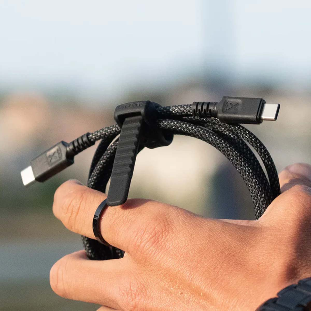 Cavo nero intrecciato con due connettori USB-C, tenuto da una mano.
