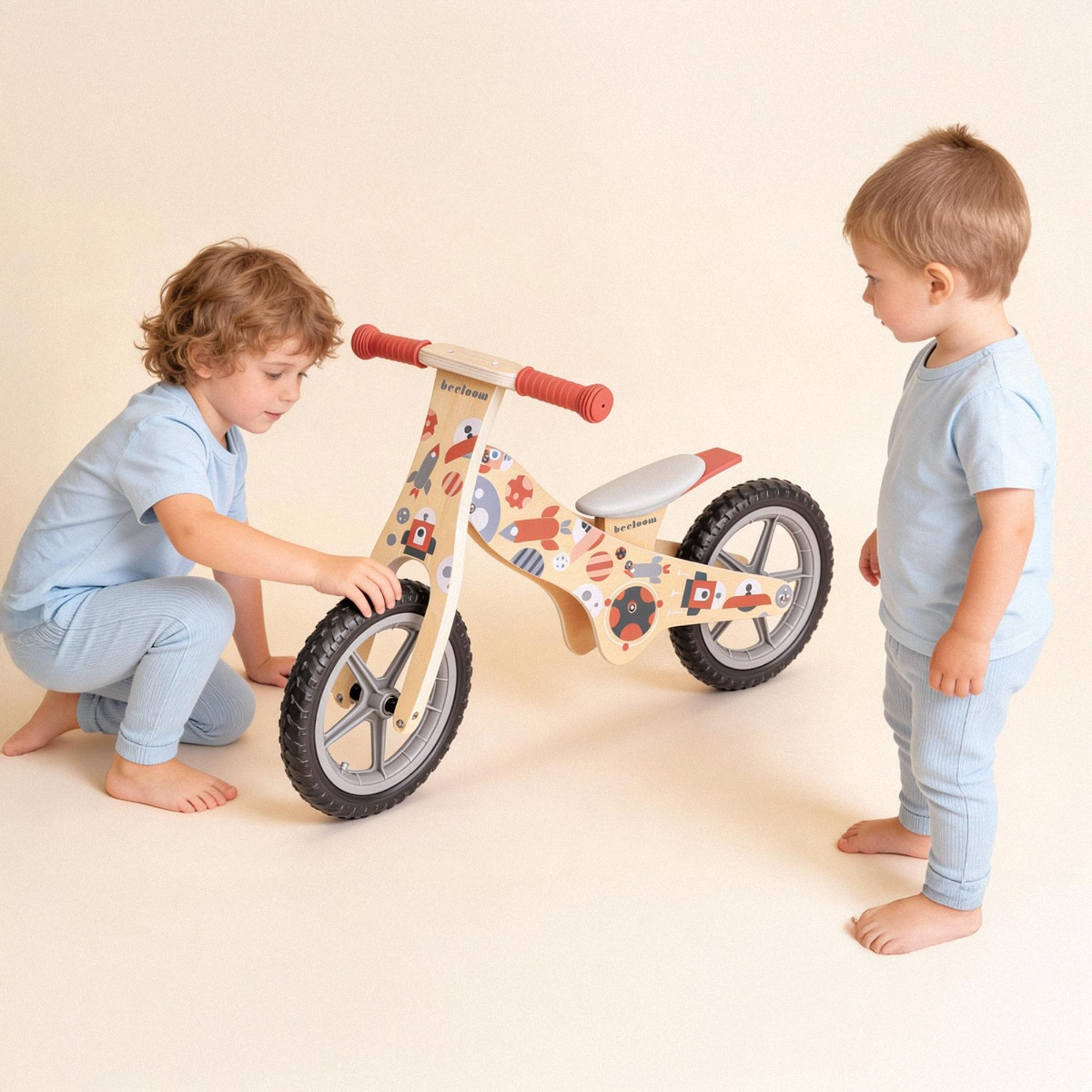 Dos niños en pijama azul miran una bicicleta de equilibrio de madera con diseños espaciales.