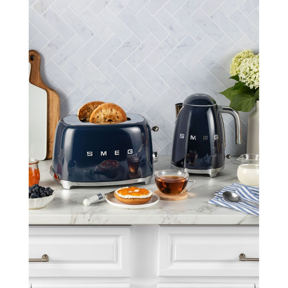 Mavi SMEG tost makinesi, üzerinde kızarmış ekmek, su ısıtıcısı, çay, simit, yaban mersini ve reçel ile.