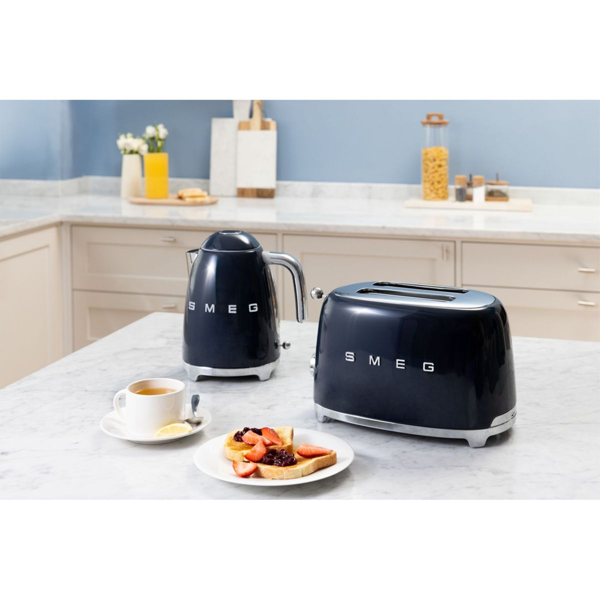 Çilek ve reçelli tostların yanında koyu mavi Smeg su ısıtıcısı ve tost makinesi.