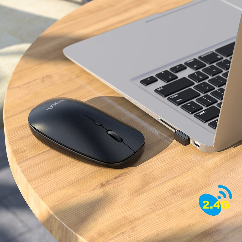 Un ratón inalámbrico negro está sobre un escritorio de madera junto a un portátil con receptor USB.