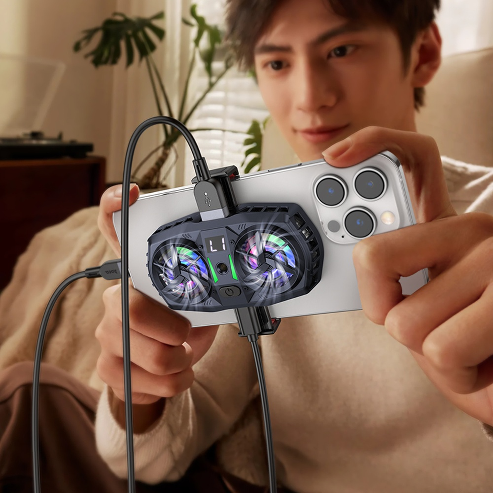 Un hombre sostiene un smartphone con un ventilador-refrigerador acoplado, conectado por cables.