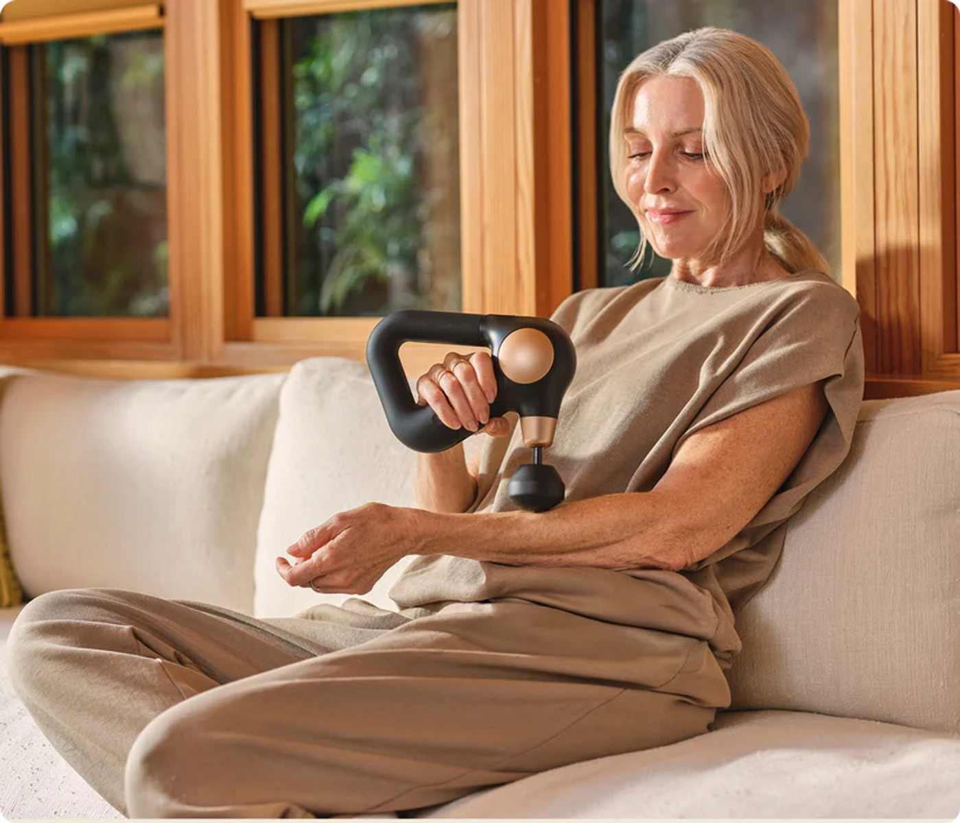 Frau auf Sofa mit Massagepistole am Arm
