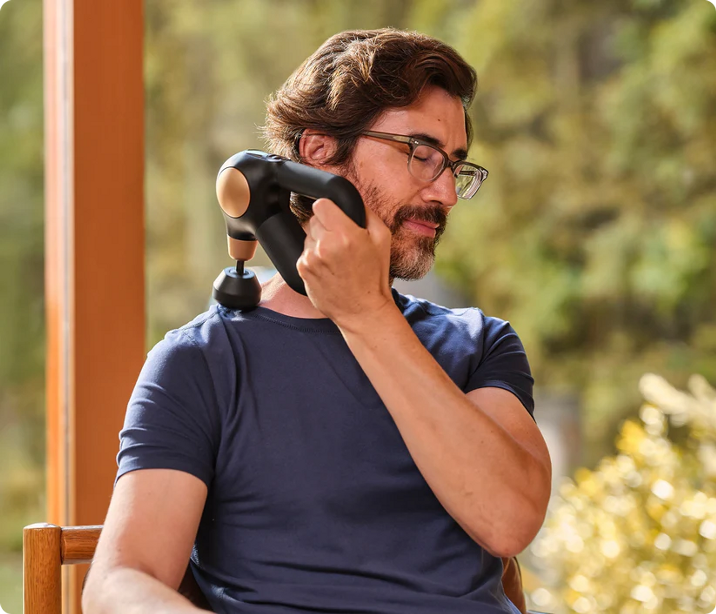 Mann mit Brille massiert Nacken mit Massagepistole im Freien.