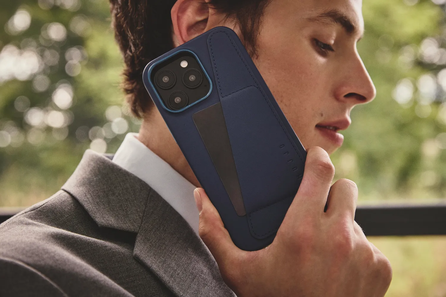 Mężczyzna w garniturze rozmawia przez ciemnoniebieskie etui na telefon. Tło bokeh.