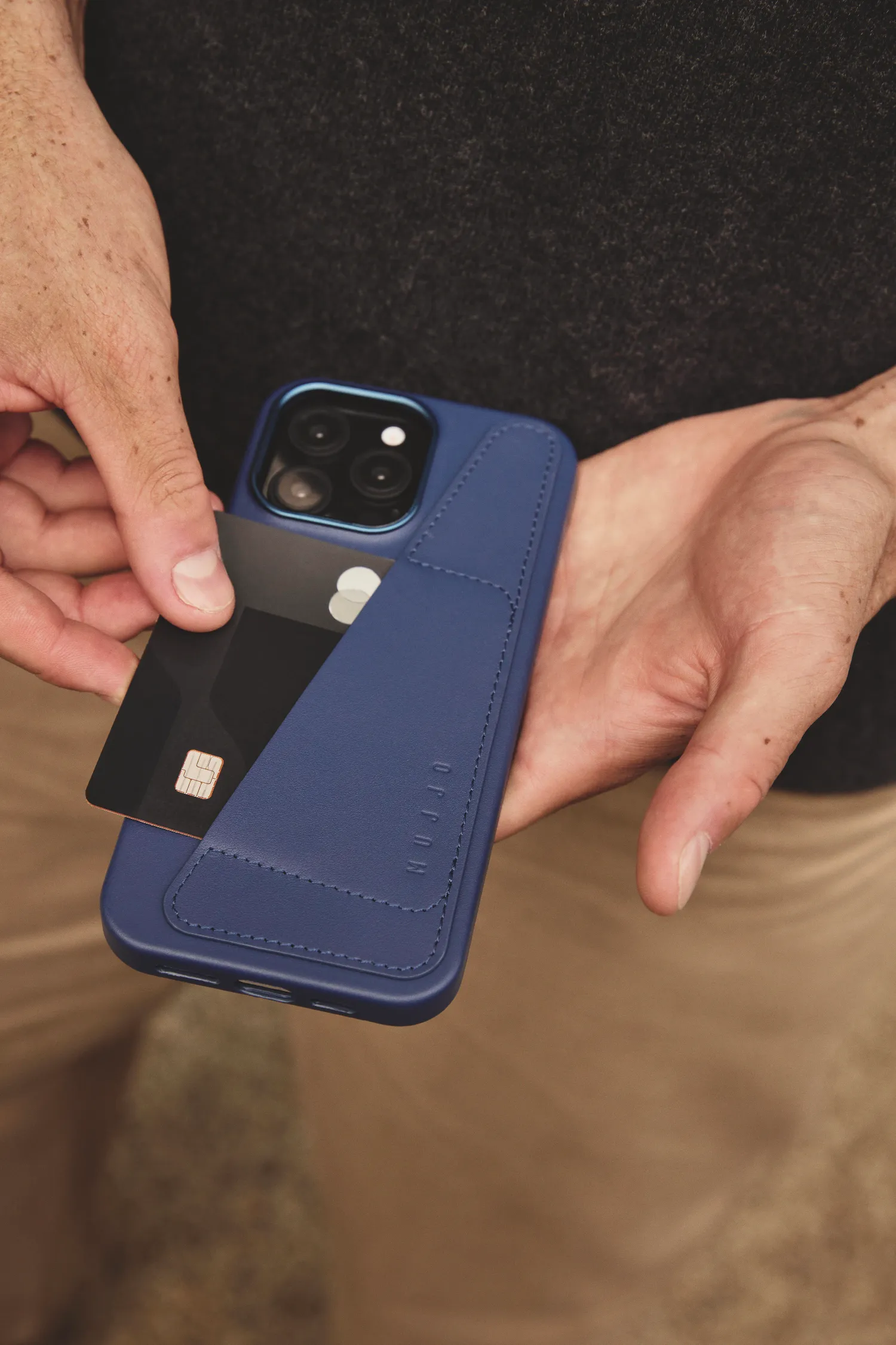 Dłoń wkłada czarną kartę kredytową do niebieskiego etui na telefon.