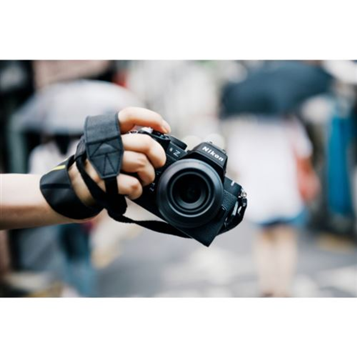 Una mano sostiene una cámara Nikon negra con correa, fondo borroso.