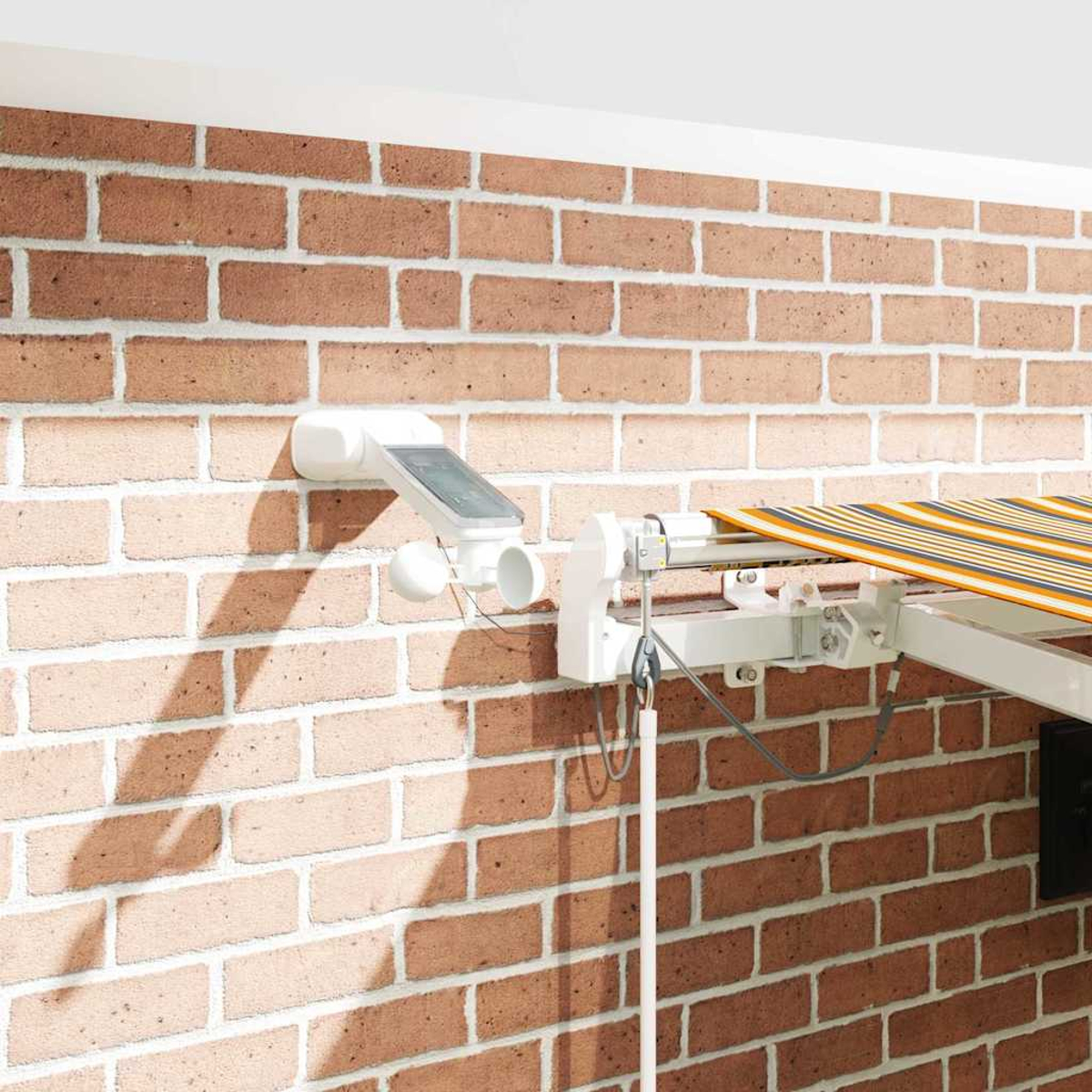 Ein weißes Markisenmodul mit Solarpanel und Windmesser an einer Ziegelwand.