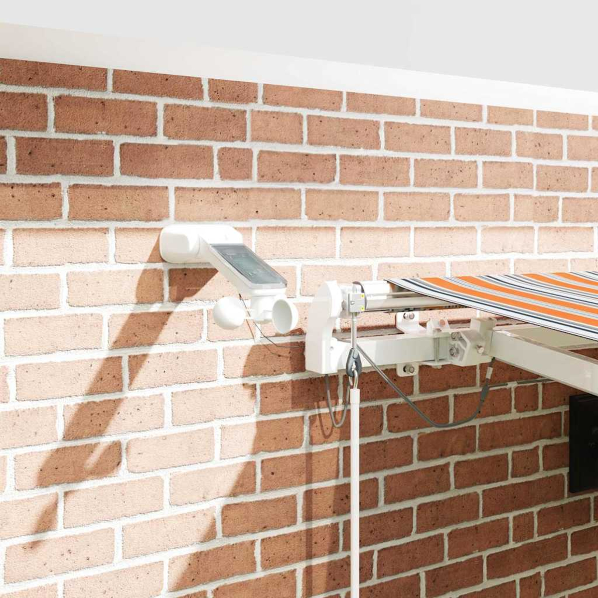 Ein weißes Markisenautomationssystem mit Solarpanel an einer Ziegelwand.
