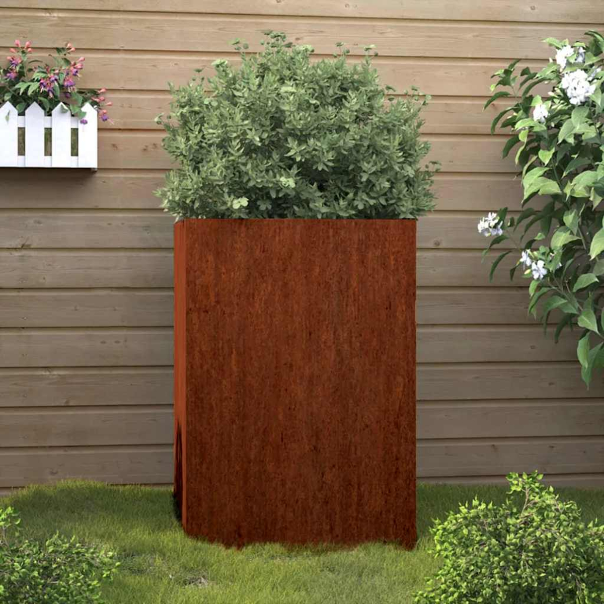 Rostiger Hochbeet-Pflanzer mit grünem Busch vor Holzwand.