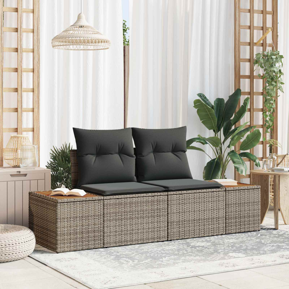 Graues Rattan-Sofa mit dunklen Kissen vor einem Fenster mit weißen Vorhängen.