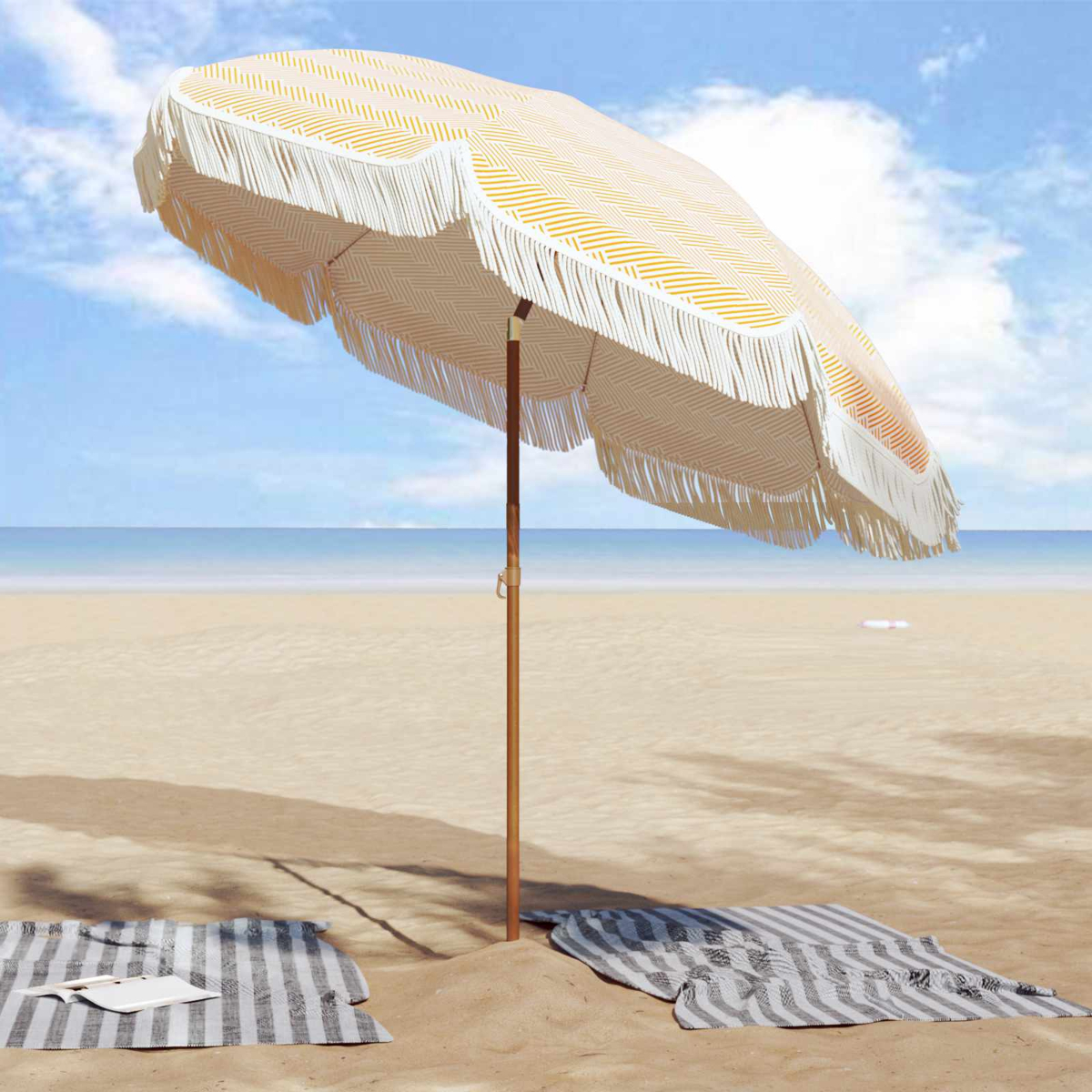 Un ombrellone da spiaggia con frange si erge sulla sabbia, con due asciugamani a righe nelle vicinanze.