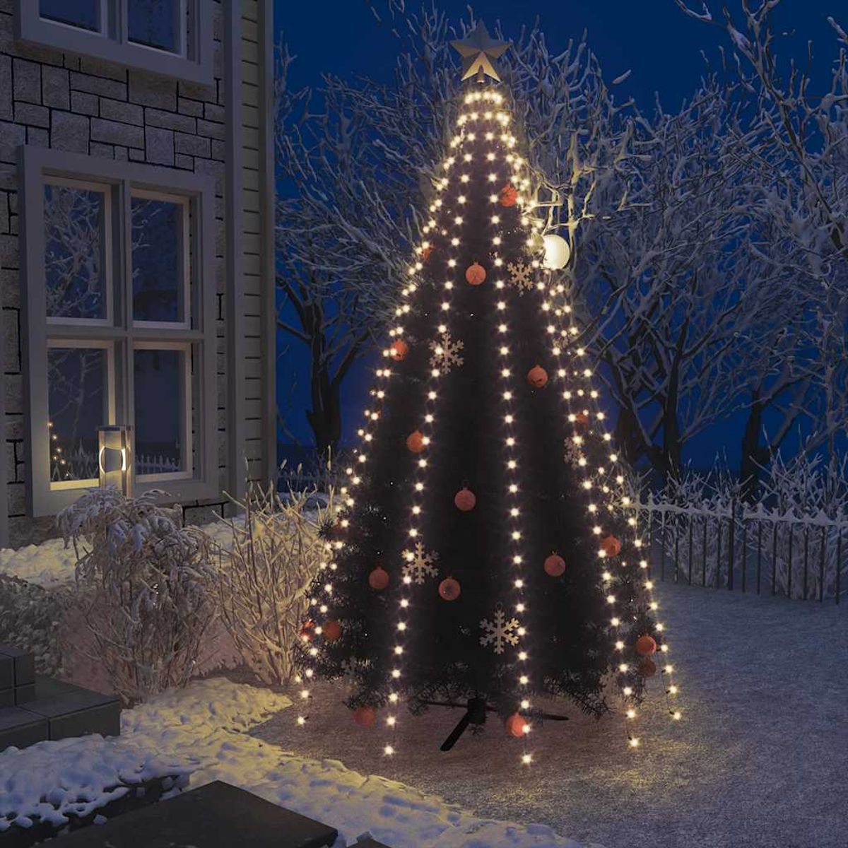 Ein beleuchteter Weihnachtsbaum mit Orangenkugeln und Schneeflocken im Schnee.
