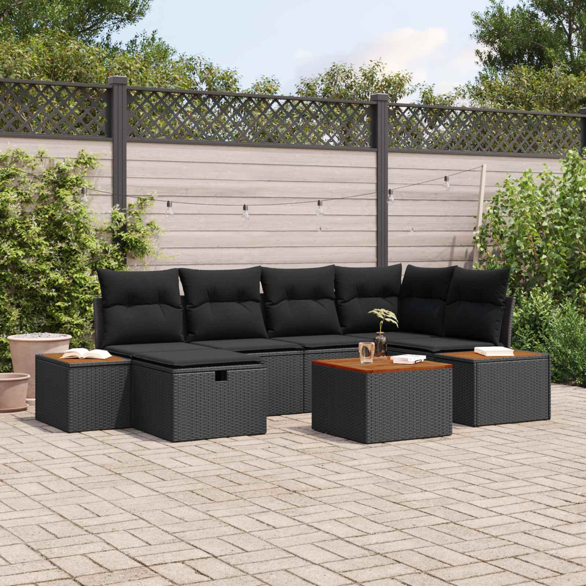 Schwarzes Polyrattan-Lounge-Set mit Kissen auf einer gepflasterten Terrasse.