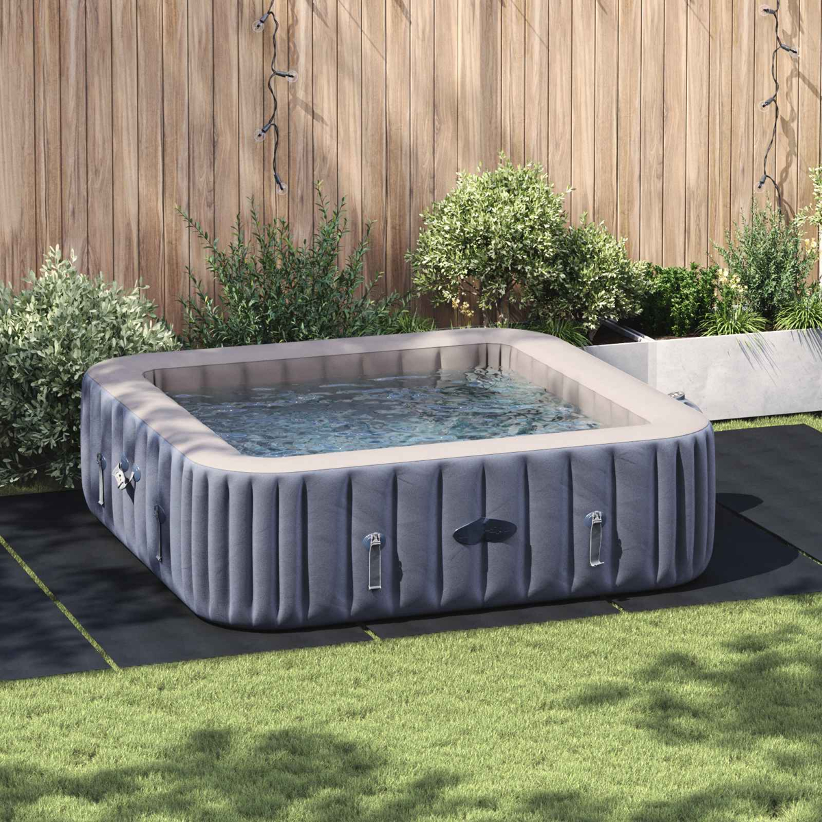 Aufblasbarer Whirlpool im Garten mit Holzzaun und Büschen im Hintergrund.