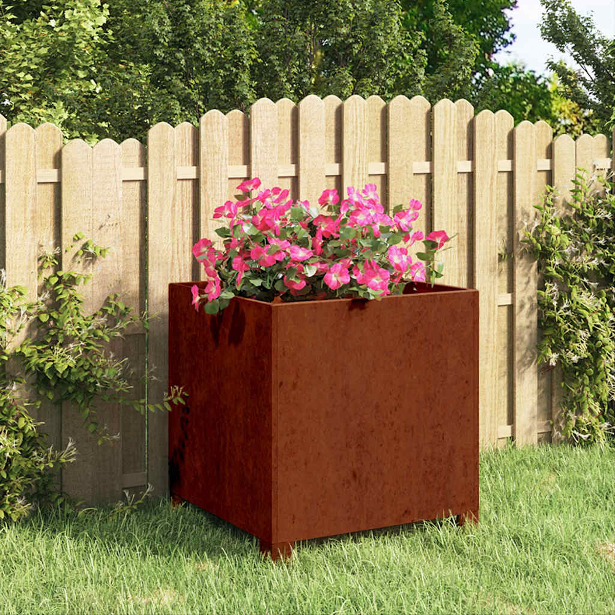 Ein brauner Metall-Blumenkasten mit rosa Blumen vor einem Holzzaun im Garten.