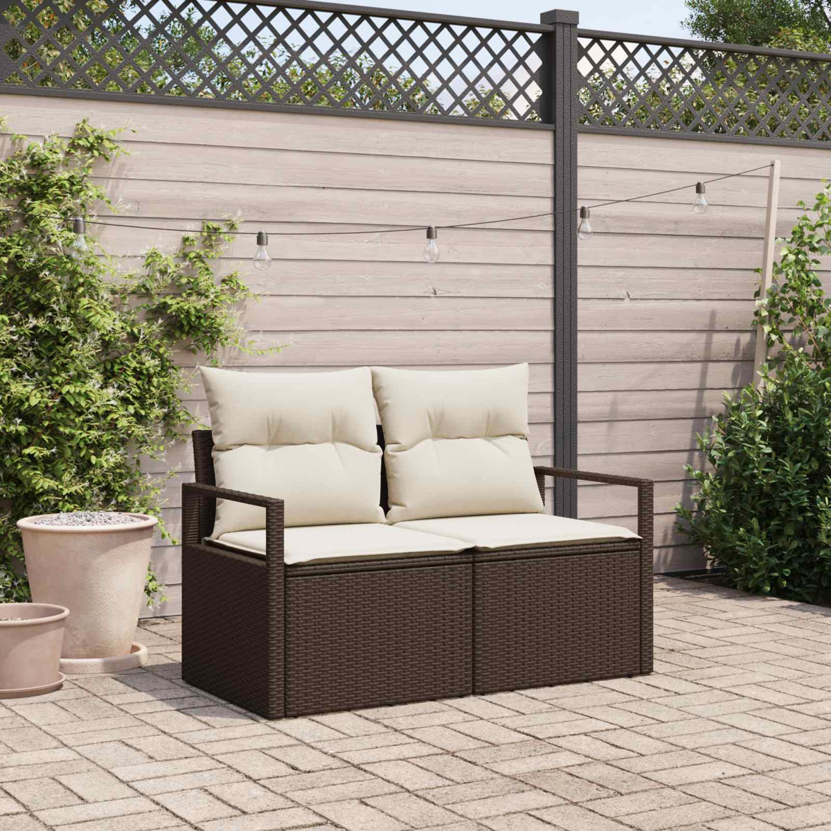 Dunkelbraunes Rattan-Sofa mit cremefarbenen Kissen auf einer gepflasterten Terrasse.