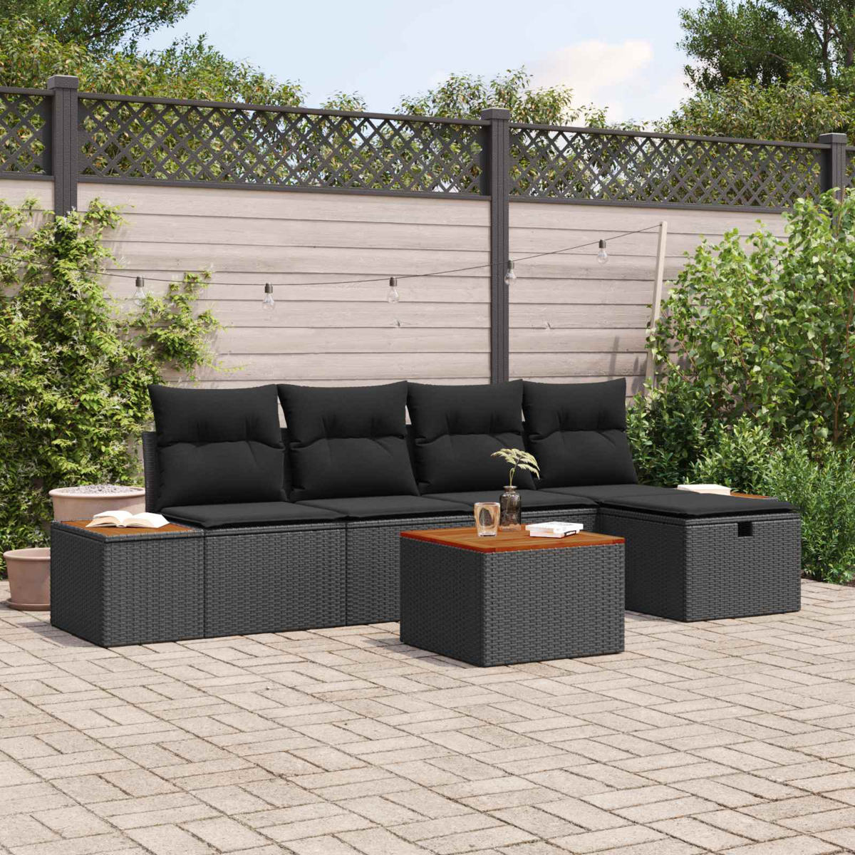Conjunto de salón exterior con mimbre gris oscuro y cojines negros en patio pavimentado.