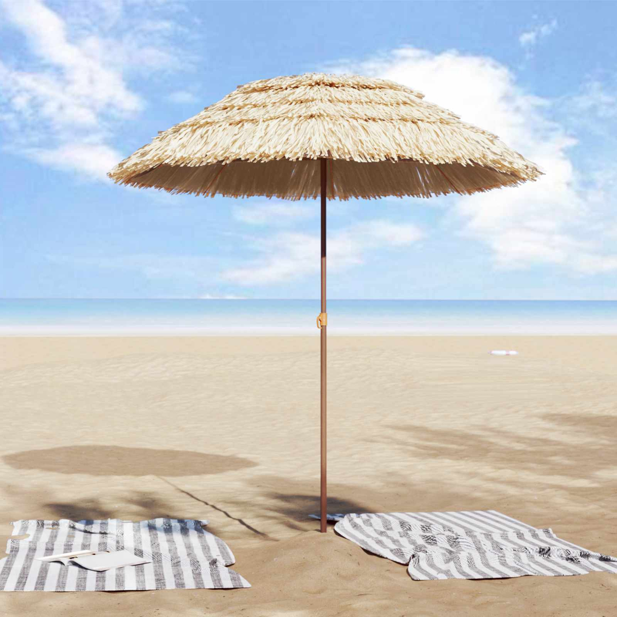 Un ombrellone di paglia sulla spiaggia con due teli mare e il mare sullo sfondo.