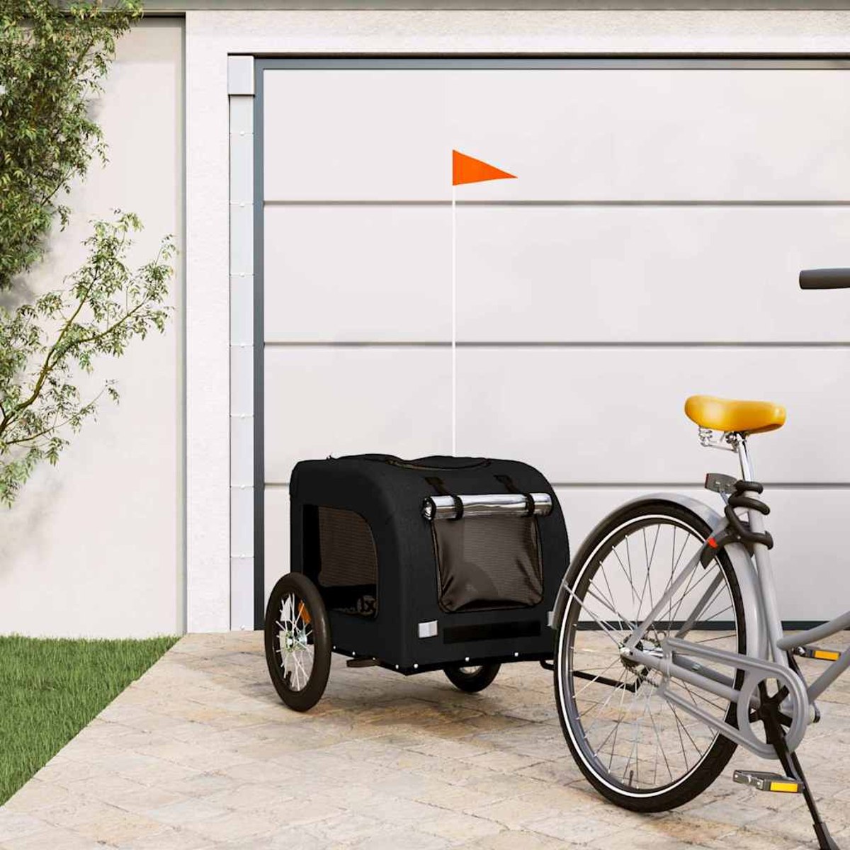 Ein schwarzer Fahrradanhänger mit orangefarbener Flagge steht neben einem Fahrrad vor einer Garage.