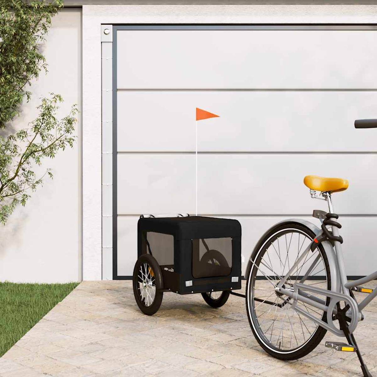 Ein graues Fahrrad mit gelbem Sattel zieht einen schwarzen Anhänger mit orangem Fähnchen vor einer Garage.