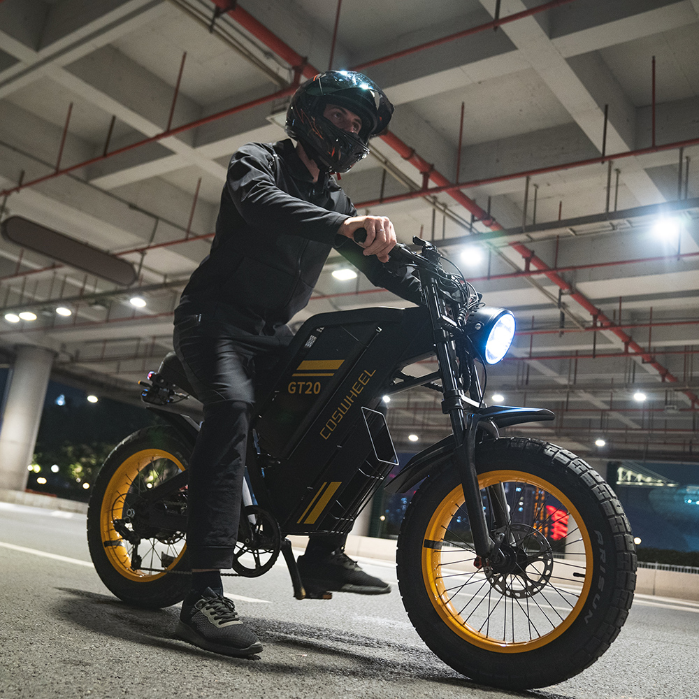 Un hombre de negro conduce una e-bike negra con llantas amarillas de noche.