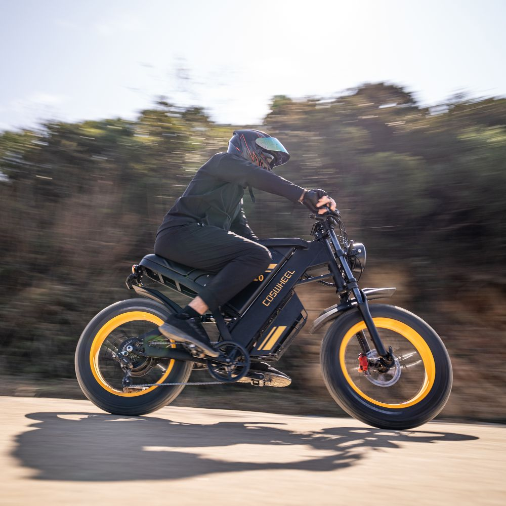 Una persona conduce una e-bike negra con llantas amarillas por una carretera.