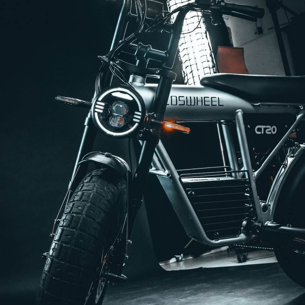 Una bici elettrica grigia con pneumatici larghi e faro LED rotondo in un luogo buio.