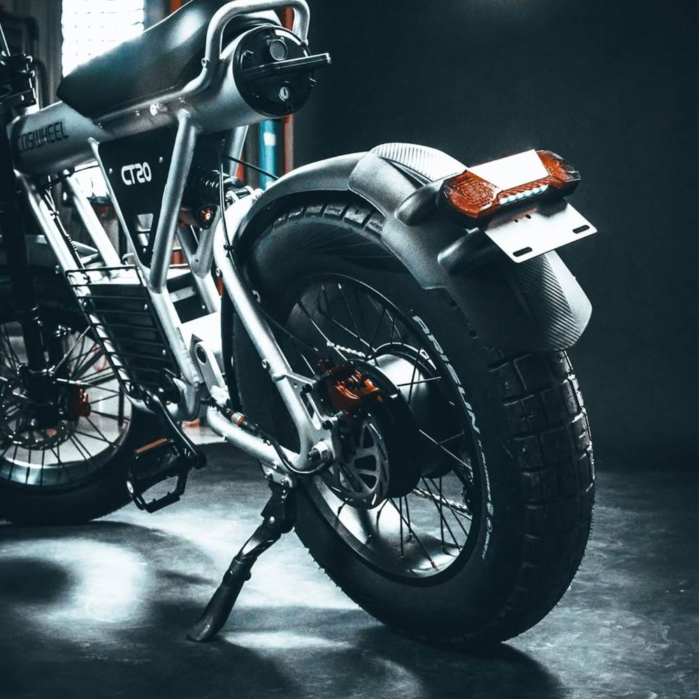 E-bike argentata con pneumatici larghi, cavalletto e fanale posteriore.
